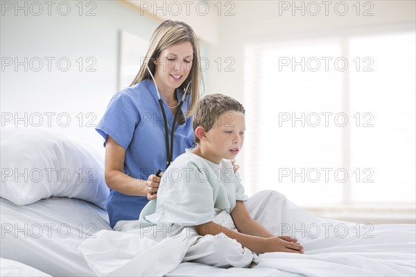 Caucasian nurse listening to chest of boy in hospital bed