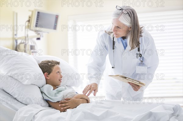Caucasian doctor talking with boy in hospital bed