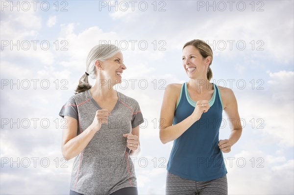 Smiling Caucasian women running against clouds