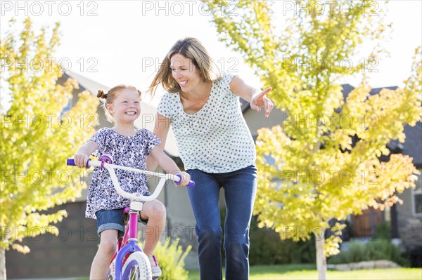 Caucasian mother teaching daughter to ride bicycle