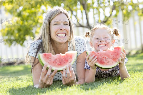 Caucasian mother and daughter laying in grass eating watermelon