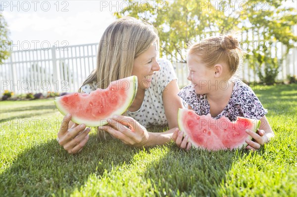 Caucasian mother and daughter laying in grass eating watermelon