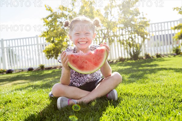 Caucasian girl sitting in grass eating watermelon