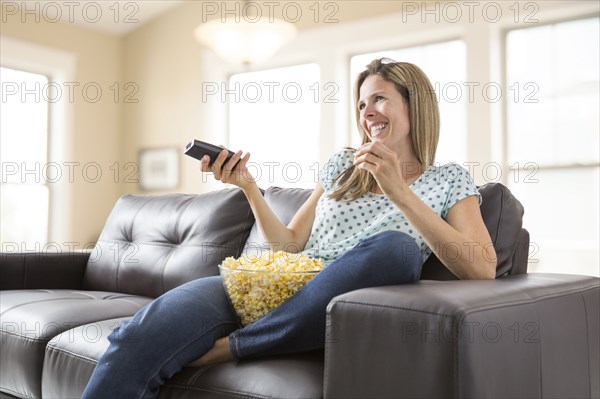 Caucasian woman watching television and eating bowl of popcorn