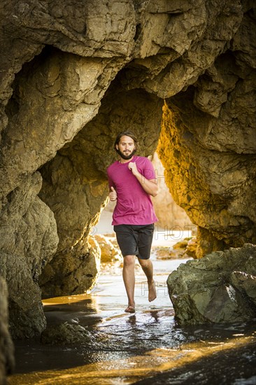 Caucasian man running under rock formation at beach