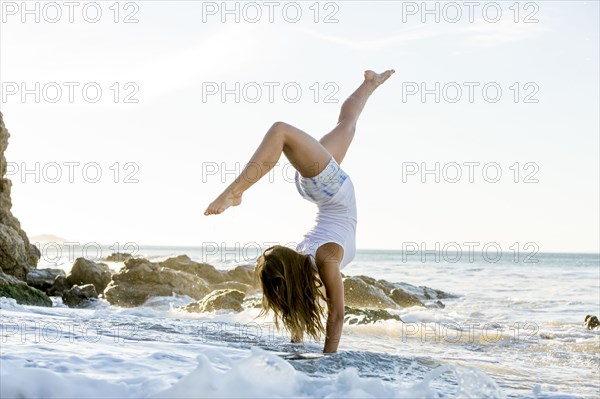 Caucasian woman doing handstand on beach