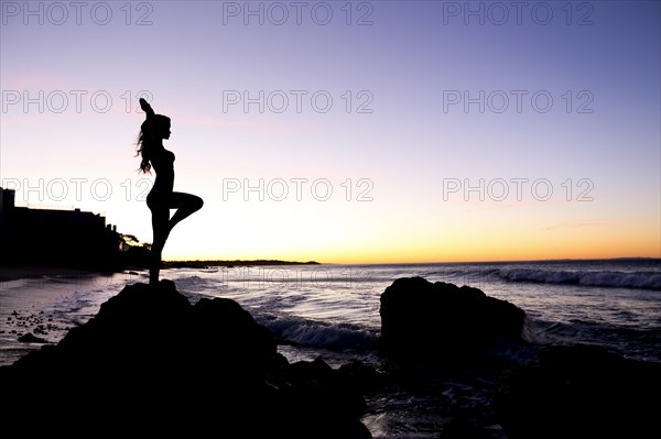 Silhouette of Caucasian woman balancing on rock at beach