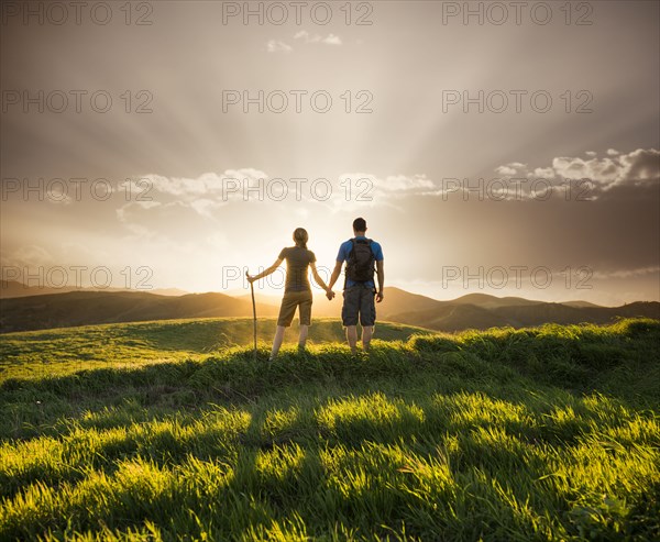 Couple holding hands on hill at sunset