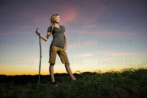 Caucasian woman holding walking stick at sunset
