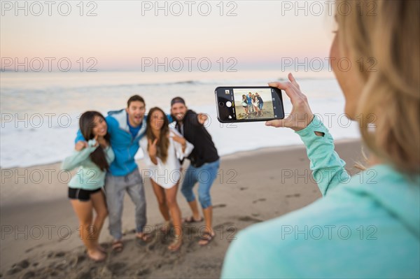 Woman photographing friends at beach with cell phone