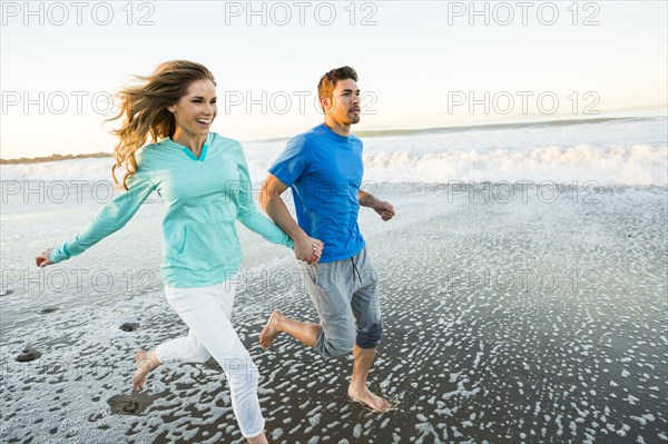 Couple holding hands running on beach