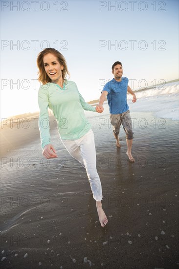 Couple holding hands running on beach