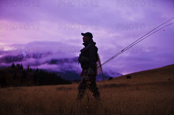 Caucasian man walking and carrying fishing rods