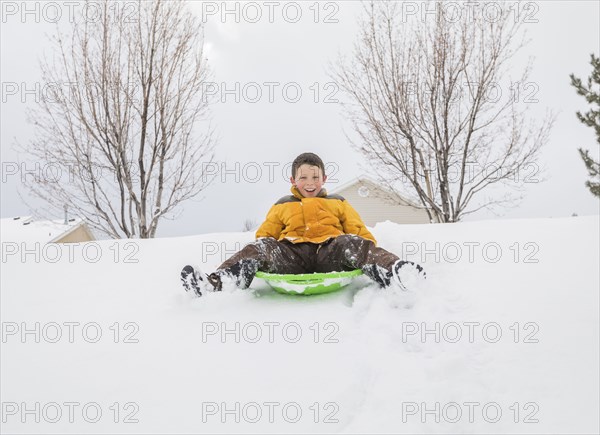 Smiling boy sliding on toboggan on hill in winter