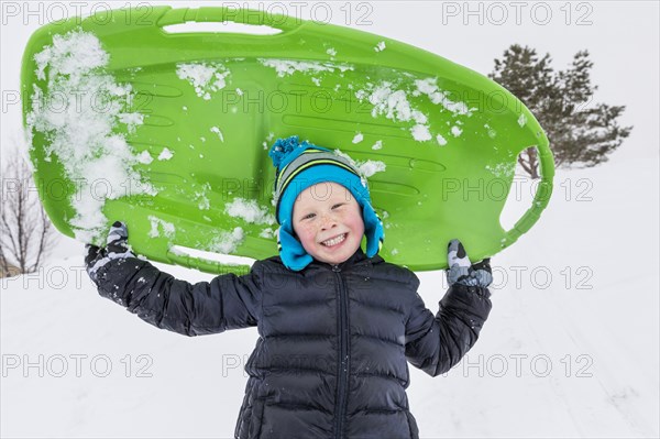 Smiling boy posing with toboggan in winter