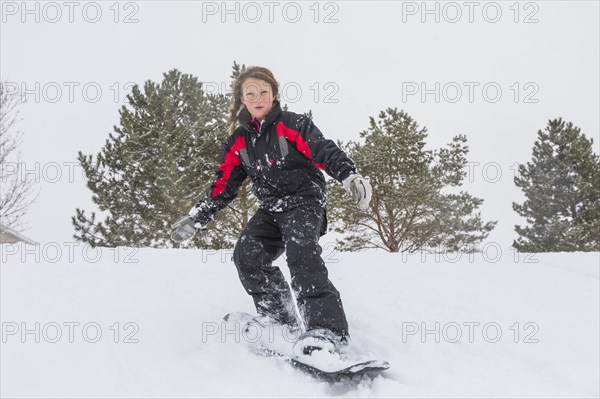 Serious girl riding snowboard on hill in winter