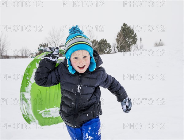 Smiling boy running with toboggan in winter