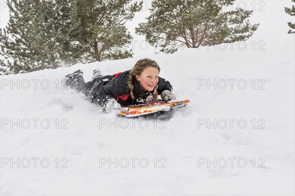 Smiling girl sliding on snowboard on hill in winter