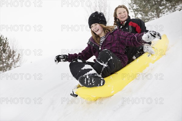 Smiling girls sliding in toboggan on hill in winter