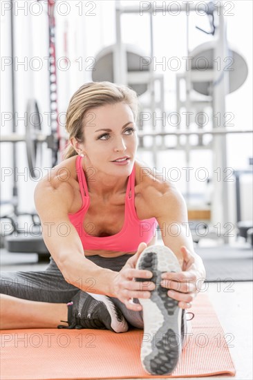 Woman stretching leg on exercise mat in gymnasium