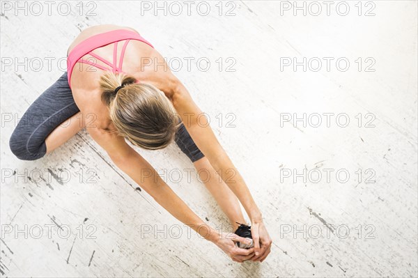 Woman sitting on wooden floor stretching leg