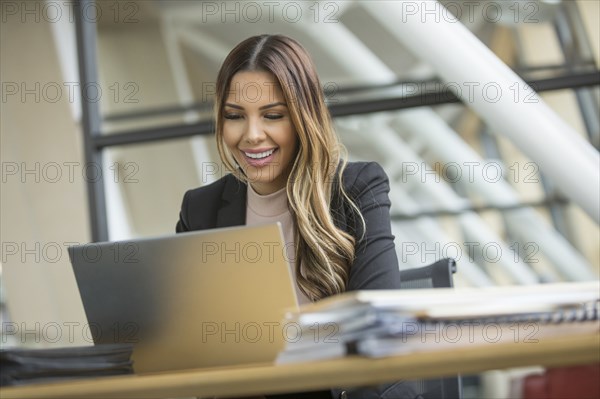 Smiling Mixed Race businesswoman using laptop