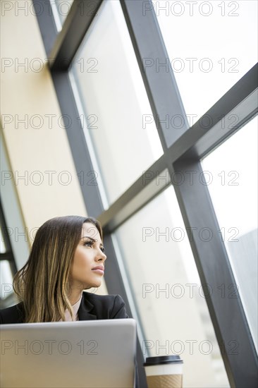 Mixed Race businesswoman with laptop daydreaming