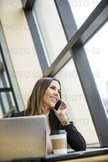 Mixed Race businesswoman talking on cell phone near laptop