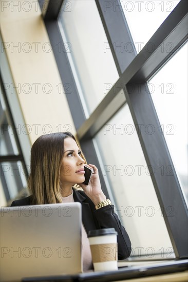 Mixed Race businesswoman talking on cell phone near laptop