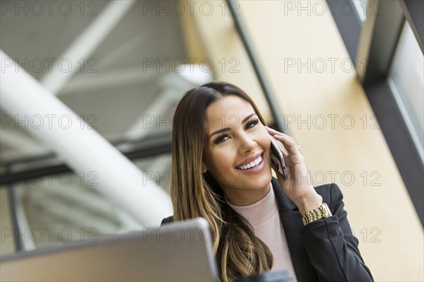 Mixed Race businesswoman talking on cell phone near laptop