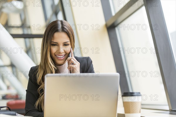 Mixed Race businesswoman talking on cell phone and using laptop