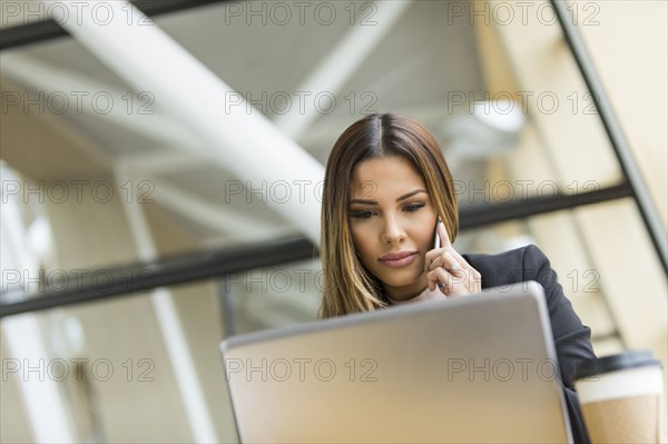 Mixed Race businesswoman talking on cell phone near laptop