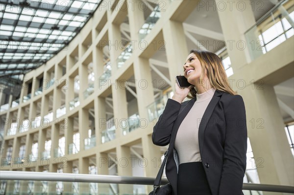 Smiling Mixed Race businesswoman talking on cell phone in lobby