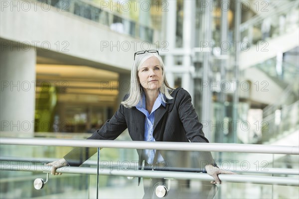 Portrait of serious Caucasian businesswoman leaning on railing in lobby