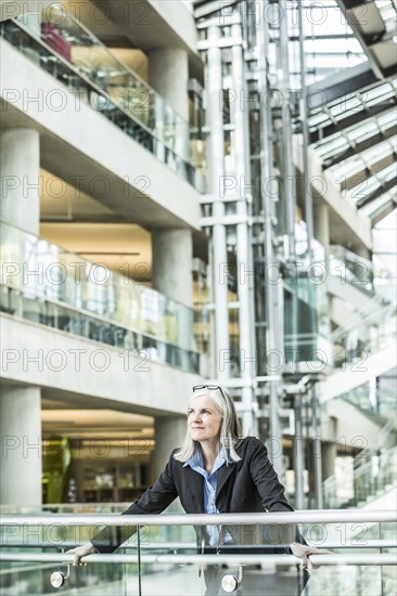 Portrait of pensive Caucasian businesswoman leaning on railing in lobby