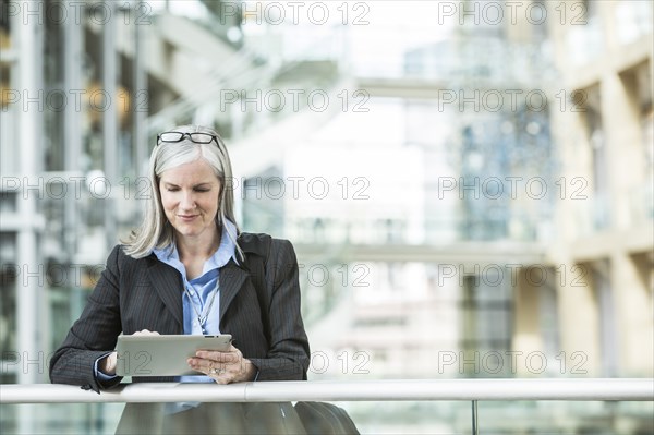 Caucasian businesswoman leaning on railing in lobby using digital tablet