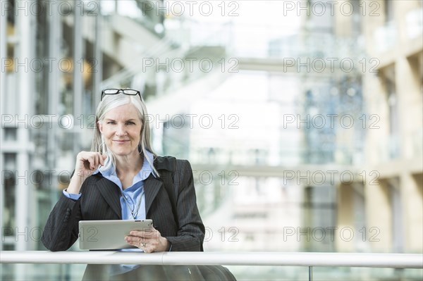 Caucasian businesswoman leaning on railing in lobby using digital tablet