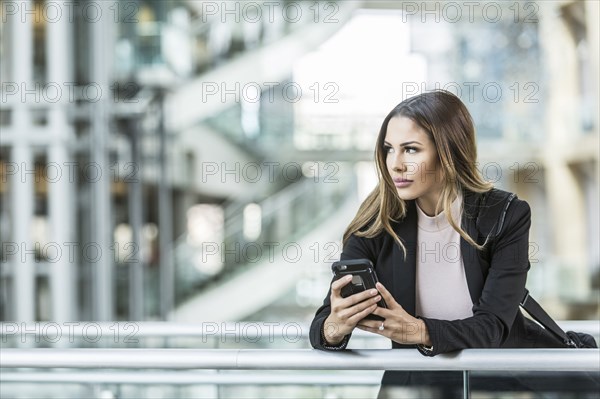 Mixed Race businesswoman texting on cell phone leaning on railing in lobby