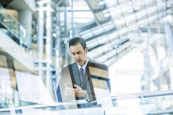 Mixed Race businessman texting on cell phone leaning on railing in lobby
