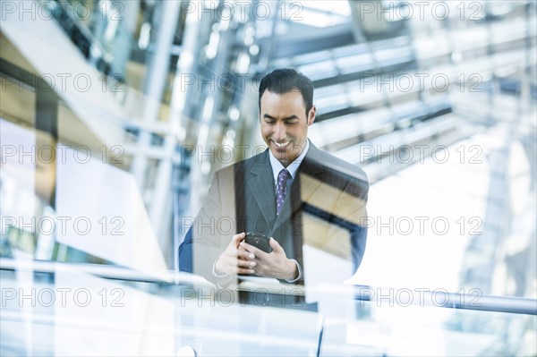 Mixed Race businessman texting on cell phone leaning on railing in lobby