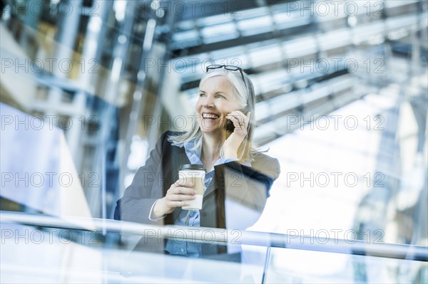 Caucasian businesswoman talking on cell phone leaning on railing in lobby