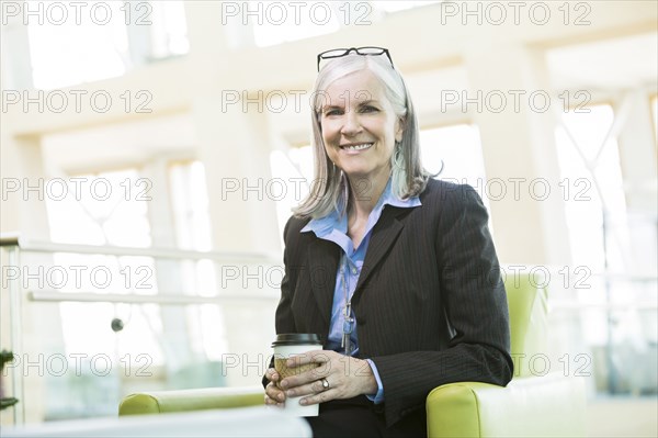 Smiling Caucasian businesswoman sitting in armchair drinking coffee