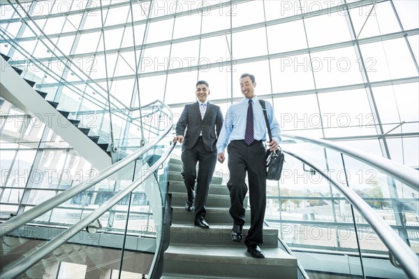 Smiling Mixed Race businessmen descending staircase