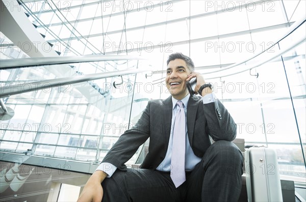 Smiling Mixed Race businessman sitting on staircase talking on cell phone
