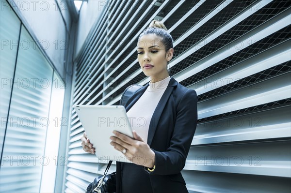 Serious Mixed Race businesswoman using digital tablet in corridor