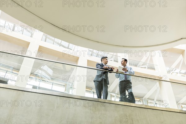 Mixed Race businessmen talking in lobby using digital tablet