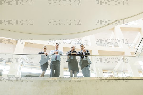 Portrait of smiling business people leaning on railing in lobby