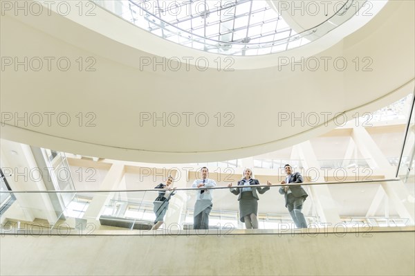 Portrait of smiling business people leaning on railing in lobby