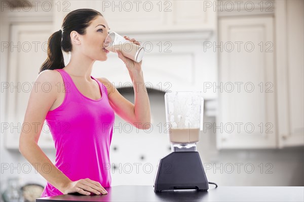 Caucasian woman drinking smoothie in kitchen