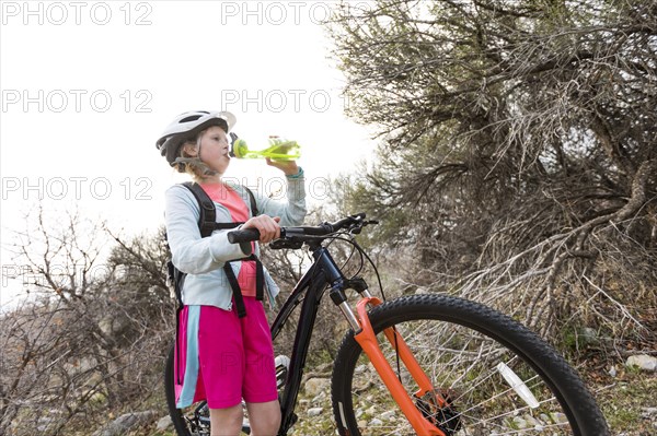 Caucasian girl holding bicycle and drinking water